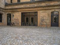 the sidewalk has a bike in front of the entrance to the building with the bicycle chained to the wall