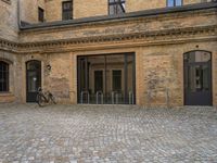 the sidewalk has a bike in front of the entrance to the building with the bicycle chained to the wall