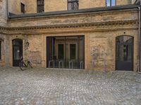 the sidewalk has a bike in front of the entrance to the building with the bicycle chained to the wall