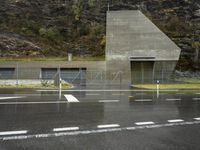 the entrance to a concrete structure near a grassy area with trees and mountains behind it