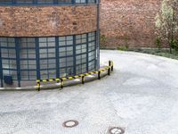 a round brick building with black windows next to a yellow and black metal pole in a parking area