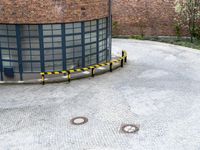 a round brick building with black windows next to a yellow and black metal pole in a parking area