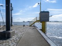 a concrete sidewalk next to the ocean near water and yellow railings with some stairs