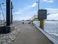 a concrete sidewalk next to the ocean near water and yellow railings with some stairs