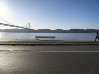 a woman running past the san francisco bridge at sunrise as the sun comes up over the bay