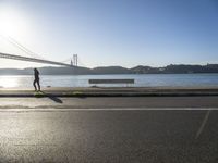 a woman running past the san francisco bridge at sunrise as the sun comes up over the bay