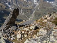 the winding mountain road is in between rocks and mountainside vegetations and a large rock formation in the foreground