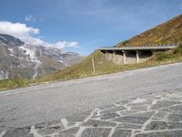 there is an empty asphalt road on the side of a mountain with snow on the mountains and green hills