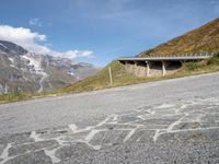 there is an empty asphalt road on the side of a mountain with snow on the mountains and green hills