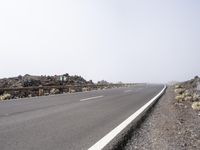 a road near the mountain side in the foggy sun day, and on the opposite bank are hills