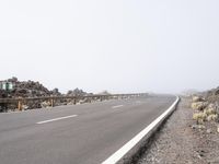 a road near the mountain side in the foggy sun day, and on the opposite bank are hills