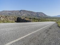 an empty road with mountains in the background and a truck sitting on it's side