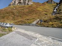 a curved mountain road with a waterfall coming down the side of it and a stop sign on the side