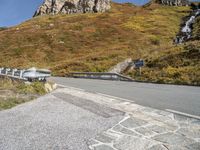 a curved mountain road with a waterfall coming down the side of it and a stop sign on the side