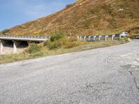 a person riding a skateboard down the side of a mountain road with a paved slope behind