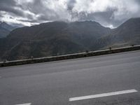 there is a person riding a bike on the road by the mountains in the rain