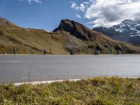 a motorcycle is parked on a road near a mountain range and snow capped peaks in the distance