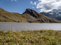 a motorcycle is parked on a road near a mountain range and snow capped peaks in the distance