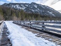 a snow covered bridge is crossing over water in the mountains near trees and snow capped hills