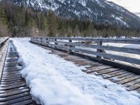 a snow covered bridge is crossing over water in the mountains near trees and snow capped hills