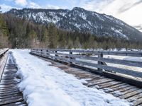 a snow covered bridge is crossing over water in the mountains near trees and snow capped hills