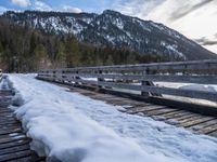 a snow covered bridge is crossing over water in the mountains near trees and snow capped hills