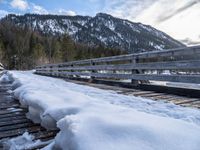 a snow covered bridge is crossing over water in the mountains near trees and snow capped hills