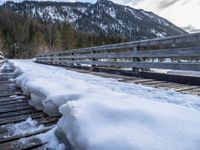 a snow covered bridge is crossing over water in the mountains near trees and snow capped hills