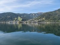 small boat out on the ocean with mountains in the background near shored lake in front of city