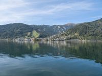 small boat out on the ocean with mountains in the background near shored lake in front of city