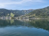 small boat out on the ocean with mountains in the background near shored lake in front of city