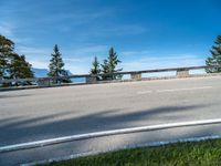 an empty highway has a wooden bench in the front of it, against a blue sky and hills