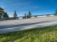 an empty highway has a wooden bench in the front of it, against a blue sky and hills