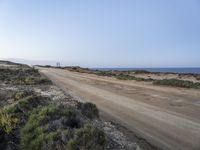 a large empty dirt road is next to the water on the shore of a beach