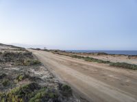 a large empty dirt road is next to the water on the shore of a beach