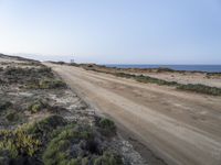 a large empty dirt road is next to the water on the shore of a beach