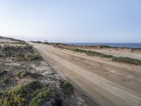 a large empty dirt road is next to the water on the shore of a beach