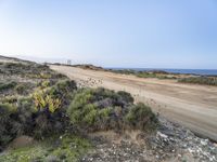 a large empty dirt road is next to the water on the shore of a beach