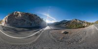 a 360 - shot looking at the road that is winding with mountains behind it and sun streaming through