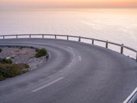 the view from above a winding road with a sunset in the background of the sea and mountains