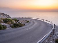 the view from above a winding road with a sunset in the background of the sea and mountains