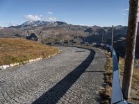 a narrow cobblestone road leading towards mountains with snow capped peaks behind it in the distance