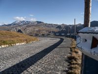 a narrow cobblestone road leading towards mountains with snow capped peaks behind it in the distance