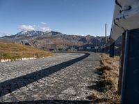 a narrow cobblestone road leading towards mountains with snow capped peaks behind it in the distance