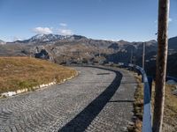 a narrow cobblestone road leading towards mountains with snow capped peaks behind it in the distance