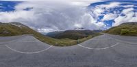 a mountain road with an upside down mirror image of the mountain and clouds are in the sky