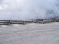 a skateboarder rides along a road past a mountain on a cloudy day with smoke