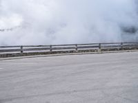 a skateboarder rides along a road past a mountain on a cloudy day with smoke