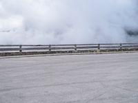 a skateboarder rides along a road past a mountain on a cloudy day with smoke