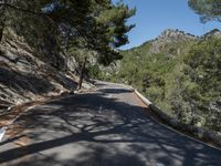 a road on the side of a mountain near trees and rocks in the shade of a tree